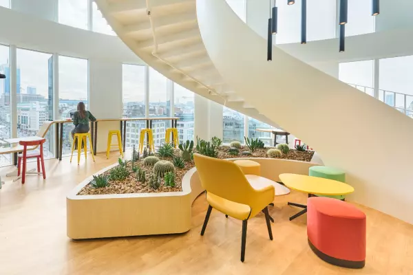 Modernes Bürointerieur mit bunten Möbeln, einem zentralen Innenbereich mit Kakteen und großen Fenstern .